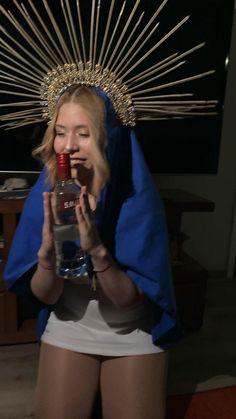 a woman wearing a headdress and holding a bottle in front of her face