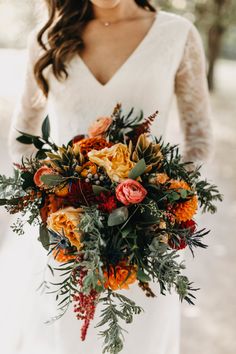 a woman holding a bouquet of flowers and greenery in her hands while wearing a white dress