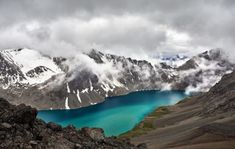 the mountains are covered with snow and blue lake in the foreground, surrounded by low lying clouds