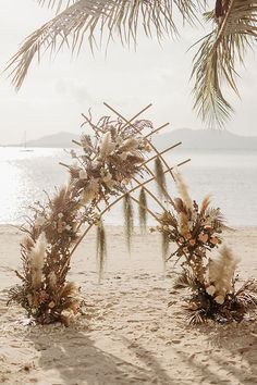 an arch made out of branches and flowers on the beach