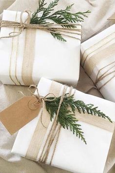 three wrapped presents tied with twine and decorated with pine needles, sitting on a bed