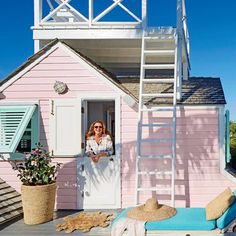 a woman standing in the doorway of a pink house with a ladder on it's side