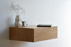 a wooden shelf with two vases and a book on it next to a white wall