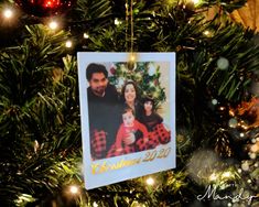 an ornament hanging on a christmas tree with lights around it and a family photo