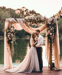 a bride and groom standing on a dock under an arch with flowers in the background