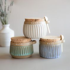 three ceramic containers with wooden handles are sitting on a table next to a white vase