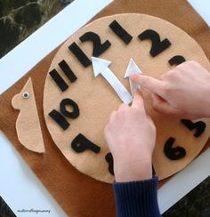 a person is making a clock out of wood and black letters on a piece of cardboard