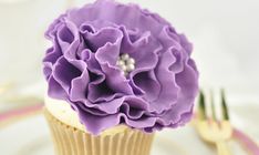 there is a cupcake with purple flowers on it and silverware next to it