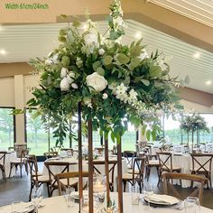 a tall centerpiece with white flowers and greenery on it in a banquet hall