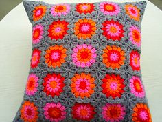 a crocheted pillow is sitting on a white chair with a pink and orange flower design