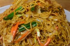 a white plate topped with noodles and veggies on top of a wooden table