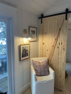 a white chair sitting in a room next to a wooden door and framed pictures on the wall