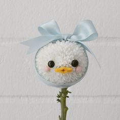 a fake white bird with a blue bow on its head sitting on top of a plant