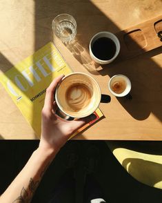 a person holding a cup of coffee on top of a wooden table next to two cups of coffee