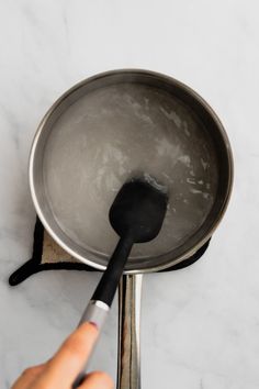 a person is stirring something in a saucepan with a spatula on the side