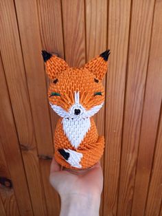 a hand holding an orange and white origami fox on top of a wooden fence