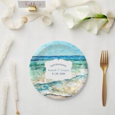 a place setting with white flowers and gold cutlery next to the table name plate