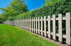 a wooden fence in the middle of a grassy area with trees and bushes behind it