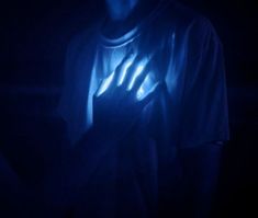 a man in the dark holding his hands up with blue light coming from behind him