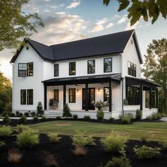 a large white house with black roof and two story windows on the second floor is surrounded by greenery