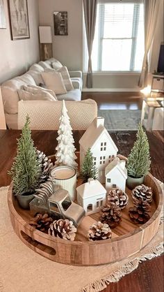 a wooden tray with pine cones and small houses on it in front of a living room window