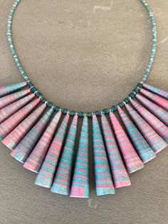 a necklace made out of pink, blue and green paper beads on a gray surface