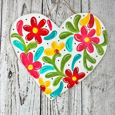 a painted heart hanging on a white wooden wall with flowers in the shape of a flower