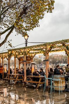 people are sitting at tables in the rain under an umbrella covered gazebo with lights on it