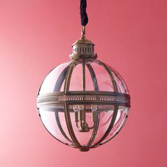 a clear glass ball hanging from a black cord on a pink wall with a light fixture in the middle