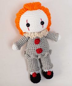 a crocheted doll with an orange hair and nose is posed on a white background