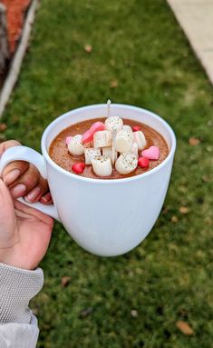 a person holding a cup filled with hot chocolate and marshmallows in it