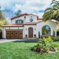 a white house with brown garage doors and palm trees in the front yard on a sunny day