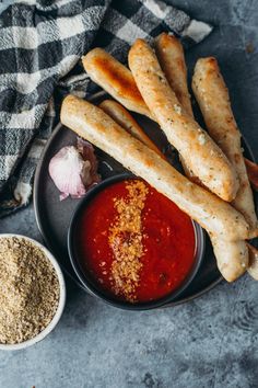 some bread sticks are sitting on a plate next to a bowl of sauce and garlic