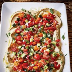 a white plate topped with an open pita bread covered in tomatoes and cucumbers