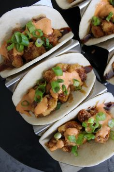 six tacos with sauce and green onions on them sitting on a plate, ready to be eaten