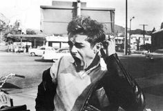 black and white photograph of a young man shouting in the street with cars behind him