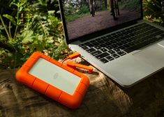 an orange case sitting on top of a wooden stump next to a laptop computer in the woods