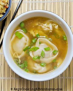 a bowl of soup with dumplings and chopsticks next to it on a bamboo mat