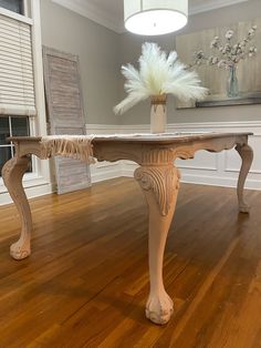 an old fashioned dining room table with feathers on it's legs, in the middle of a wood floor