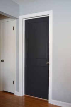 an empty room with a black door and hard wood flooring in front of it