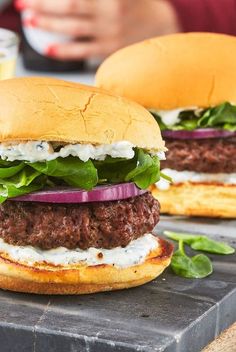 two hamburgers with lettuce, onions and cheese on them sitting on a slate slab