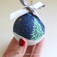 a hand holding a painted ornament with a christmas tree on it's side