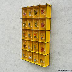 a yellow wall mounted display case filled with lots of glass cups and magnets on it's sides