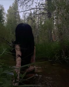 a woman standing in the water with her back turned to the camera and trees behind her