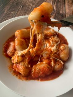 a white plate topped with pasta and meat covered in sauce on top of a wooden table