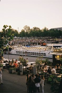 a group of people sitting at tables in front of a large white boat on the water