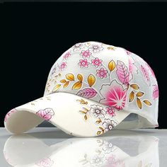 a white hat with pink and yellow flowers on the front, sitting on top of a reflective surface