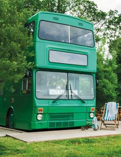 a green double decker bus parked in front of a building with chairs around the outside