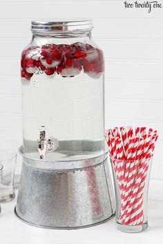 a glass jar filled with candy canes on top of a white counter next to two cups