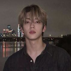 a young man standing in front of a body of water with a city skyline behind him